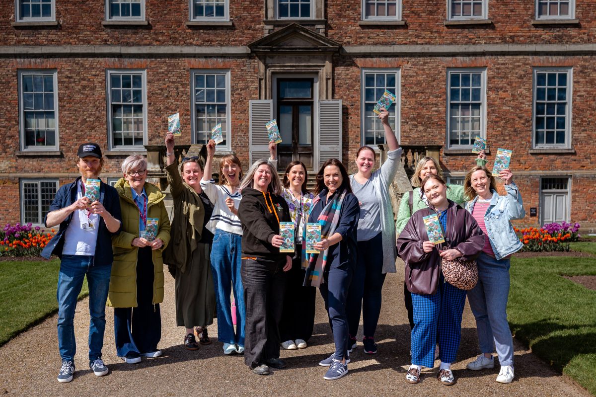 Group of people in front of a historic red brick country house holding copies of the visitor attractions leaflets