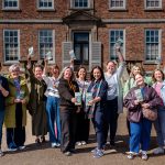 Group of people in front of a historic red brick country house holding copies of the visitor attractions leaflets